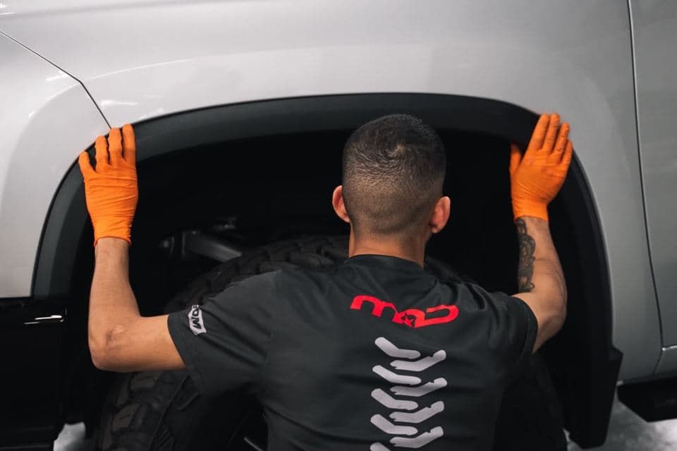 A technician in a MAD Custom shirt checking wheel-well clearance on a Silverado 2500 HD
