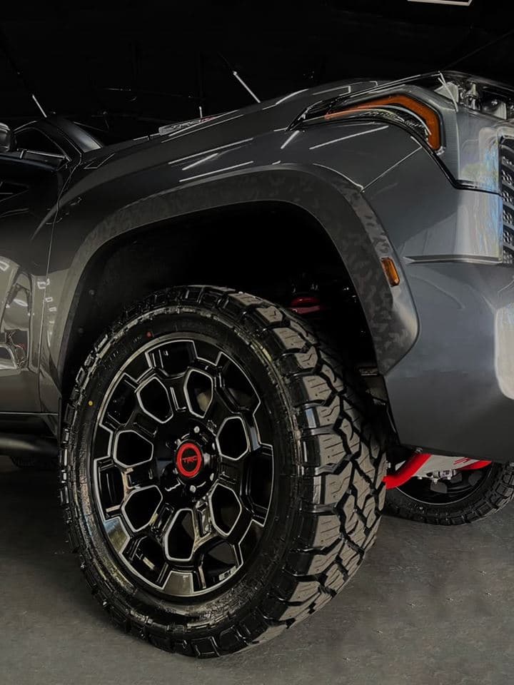 The front wheel arch of a grey Toyota Tundra TRD Pro on a black TRD wheel and all-terrain tire inside the shop