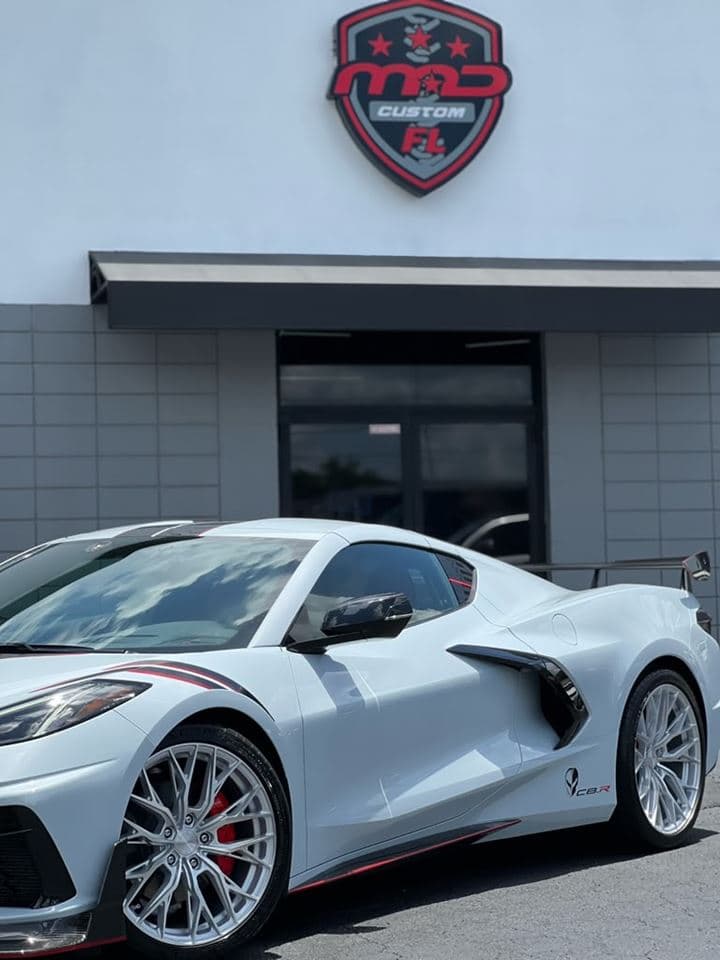 A white Corvette C8.R Edition parked outside the MAD Custom Florida shop beneath the MAD shield sign